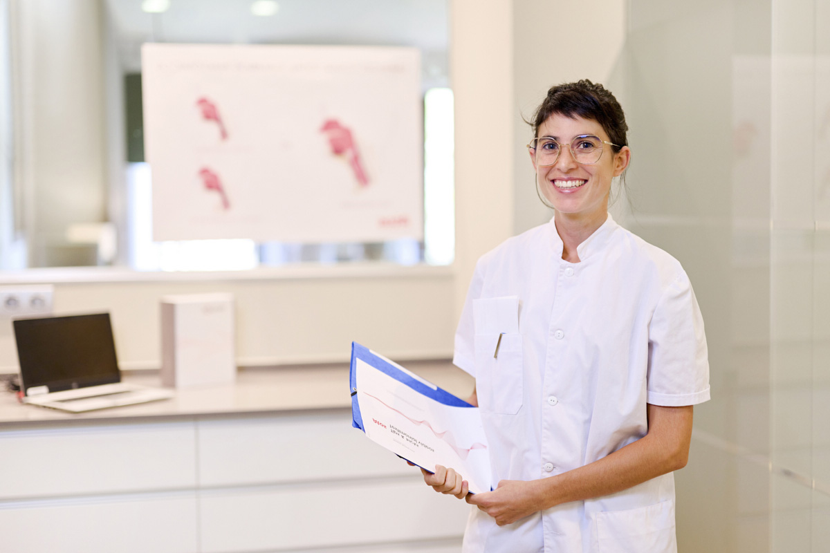 Healthcare Professional stands in office holding papers while smiling.