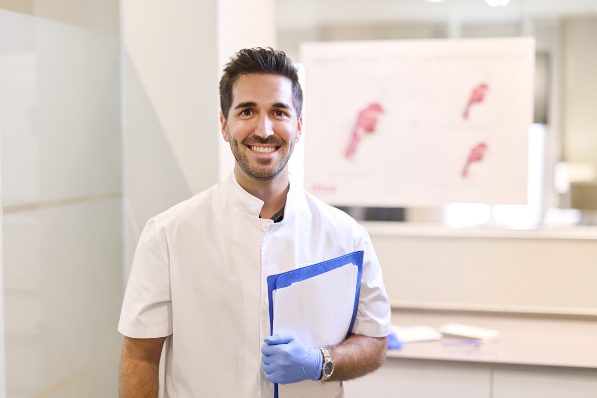 Healthcare Professional stands in office holding papers while smiling.